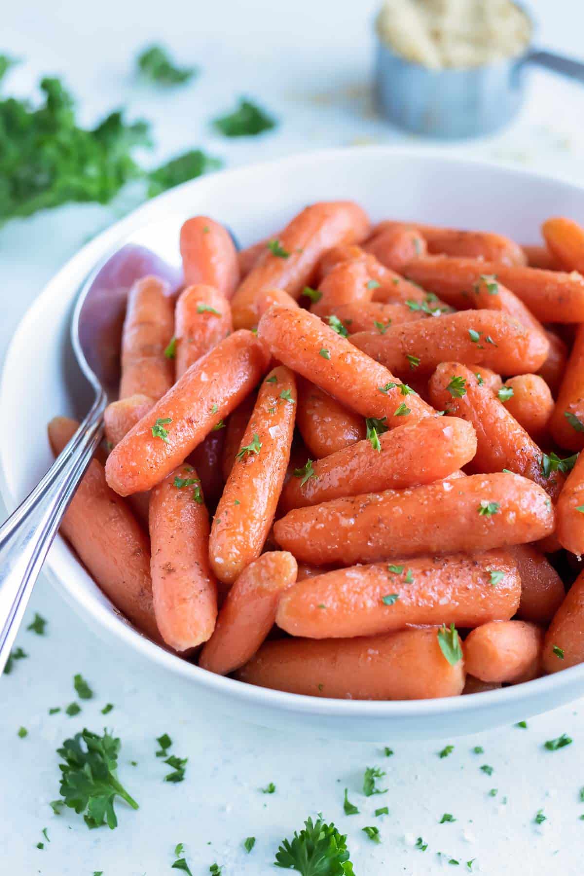 Glazed carrots made in the pressure cooker are served in a white bowl with a spoon.