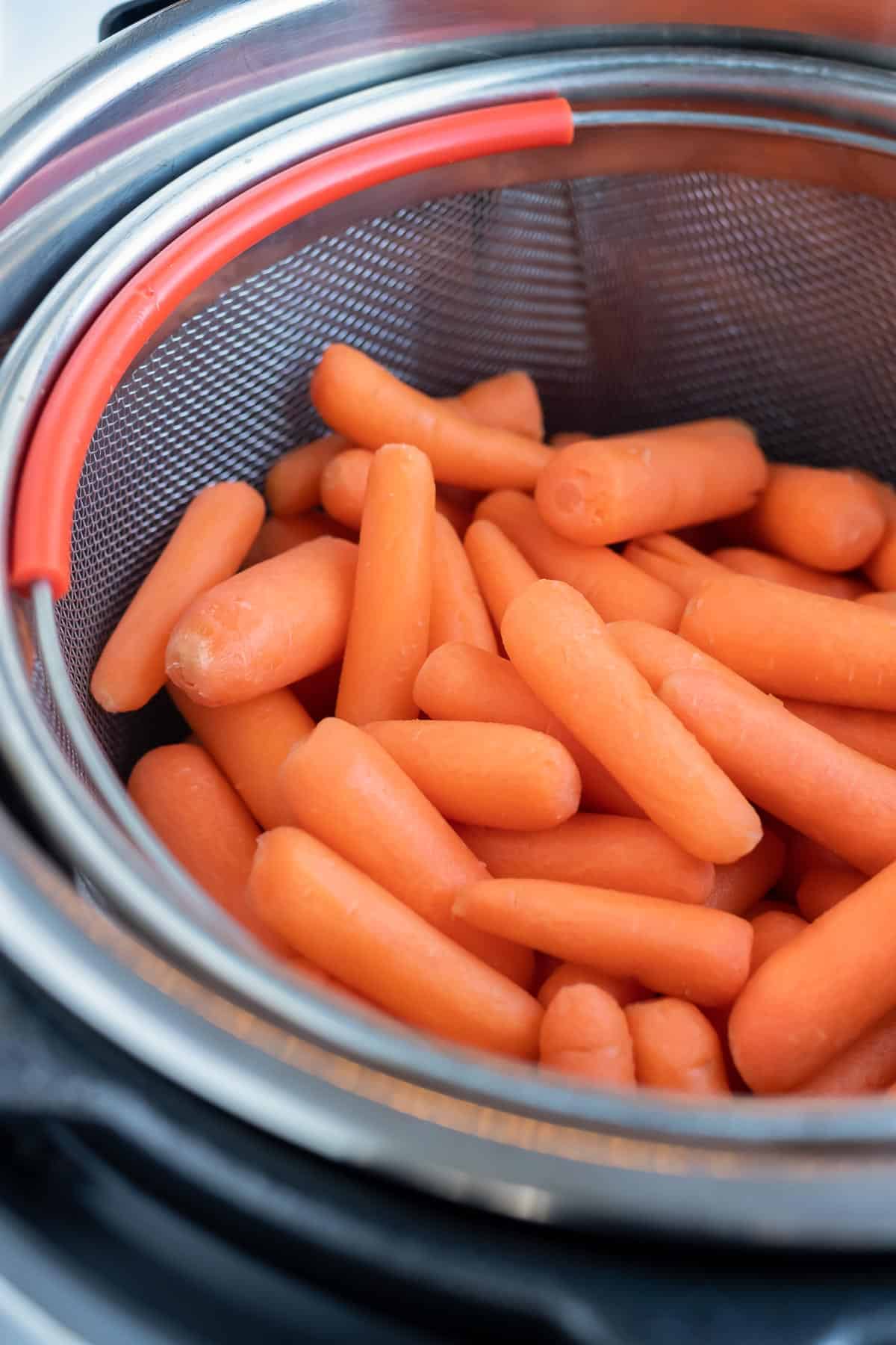 Baby carrots in a strainer are placed inside the isntant pot.