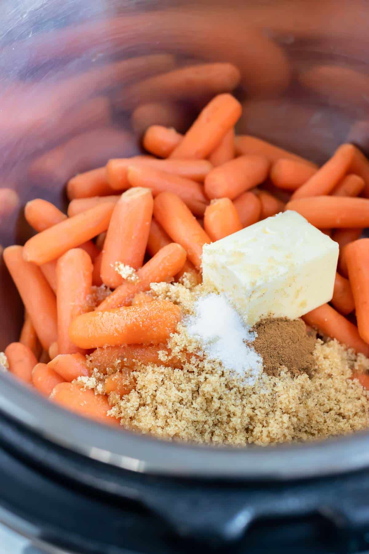 Butter, sugar, and seasonings are placed on the baby carrots in the instant pot.