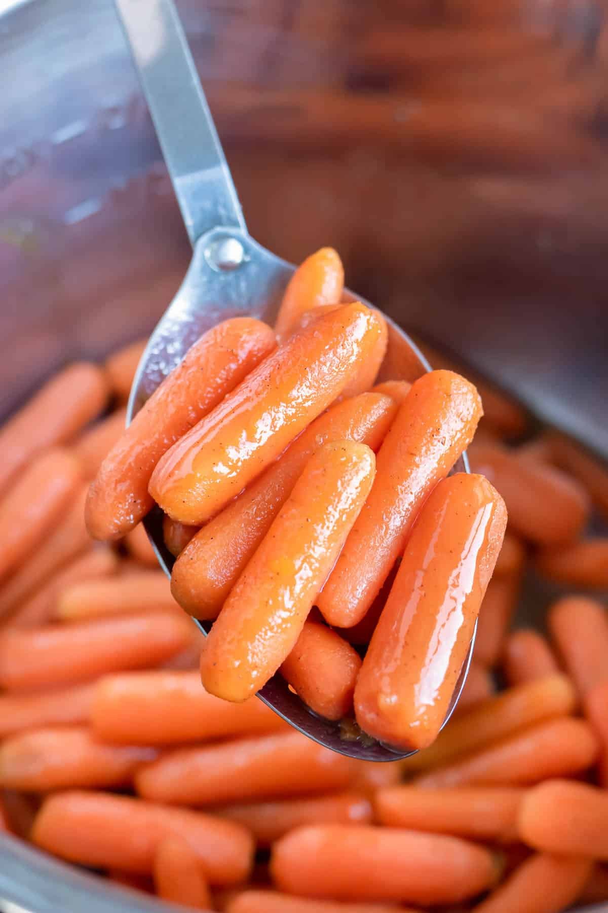 Glazed carrots are lifted out of the instant pot by a metal spoon.