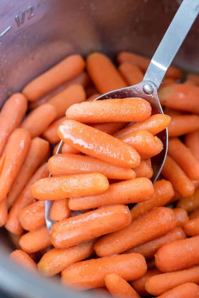 A metal spoon is used to lift brown sugar glazed carrots out of the instant pot.