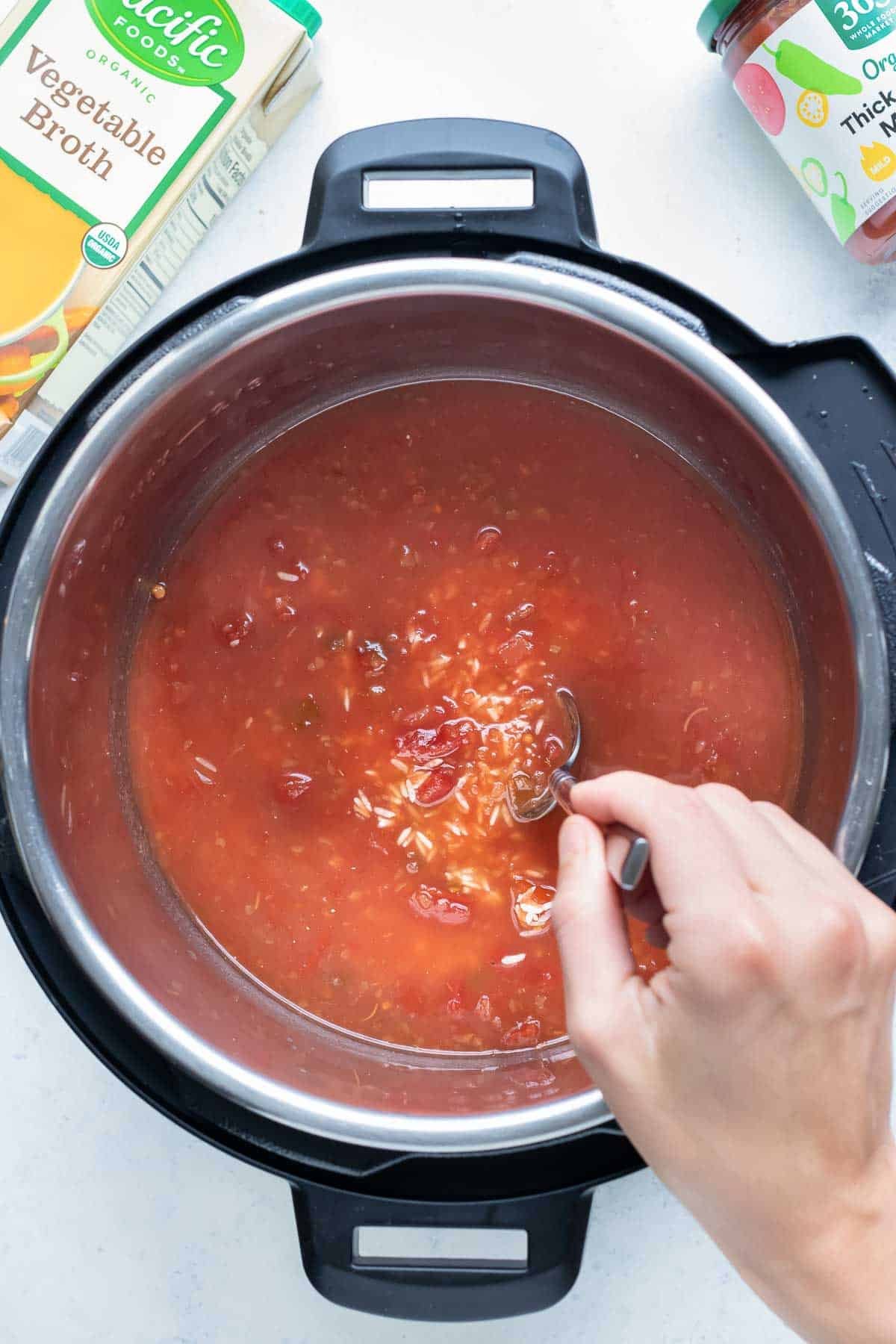Rice, vegetable broth, and tomato paste are combined in a pressure cooker.