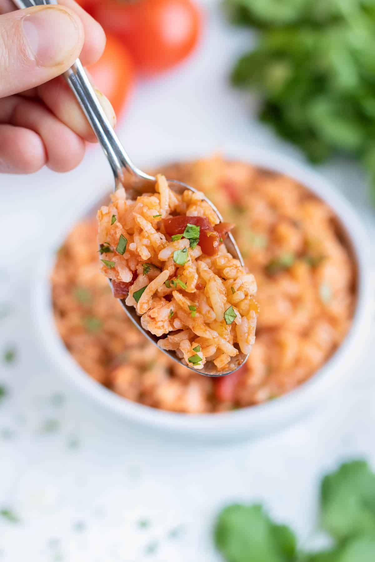 A metal spoon full of pressure cooker Mexican rice is lifted up from the bowl.