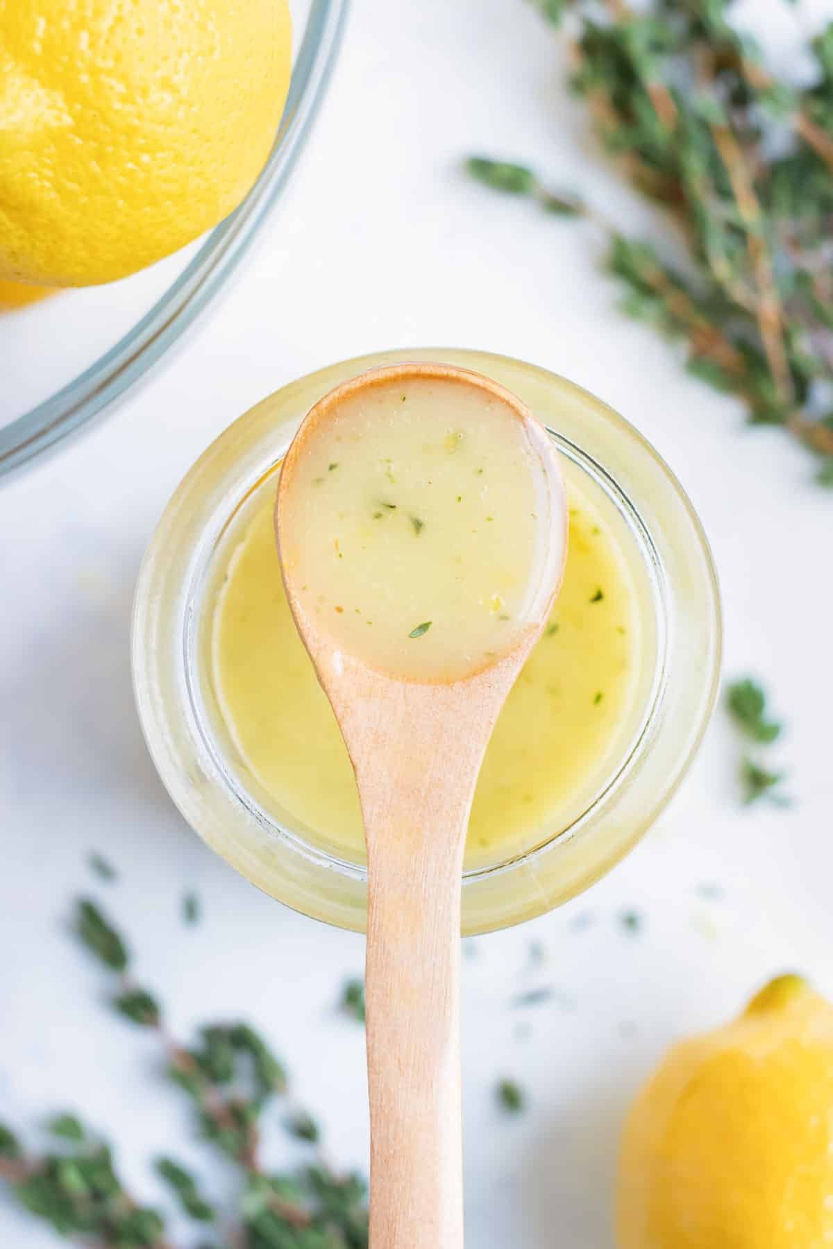 Lemon vinaigrette is kept in a jar on the counter with fresh herbs and lemons.