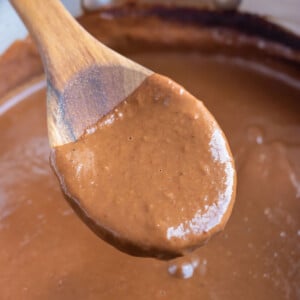 A wooden spoon lifts up an easy mole sauce from a metal saucepan.