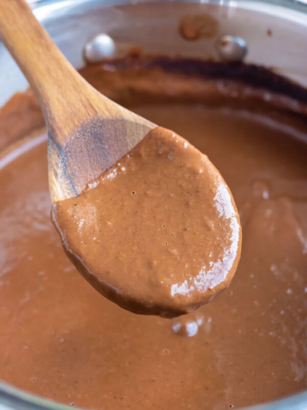 A wooden spoon lifts up an easy mole sauce from a metal saucepan.