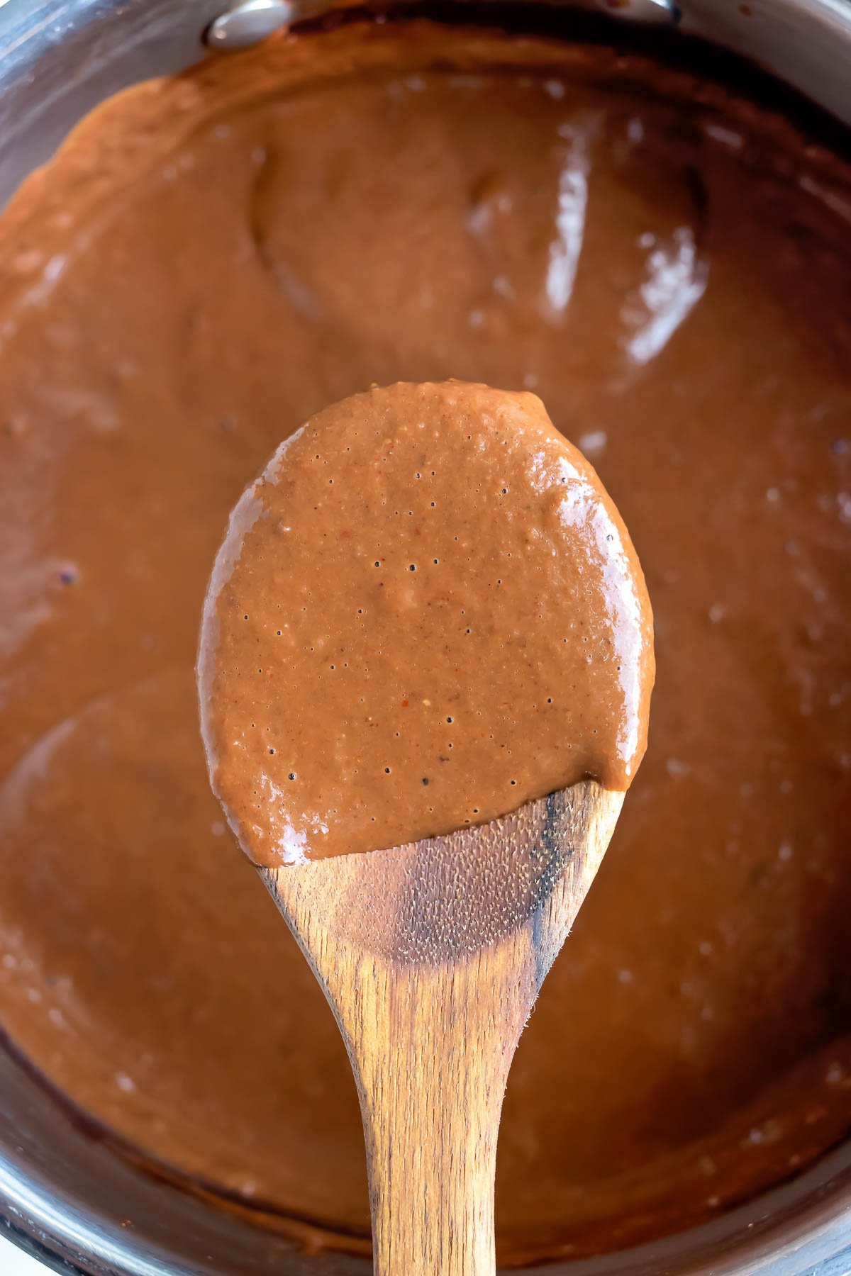 Mole sauce is lifted out of a pot with a wooden spoon.