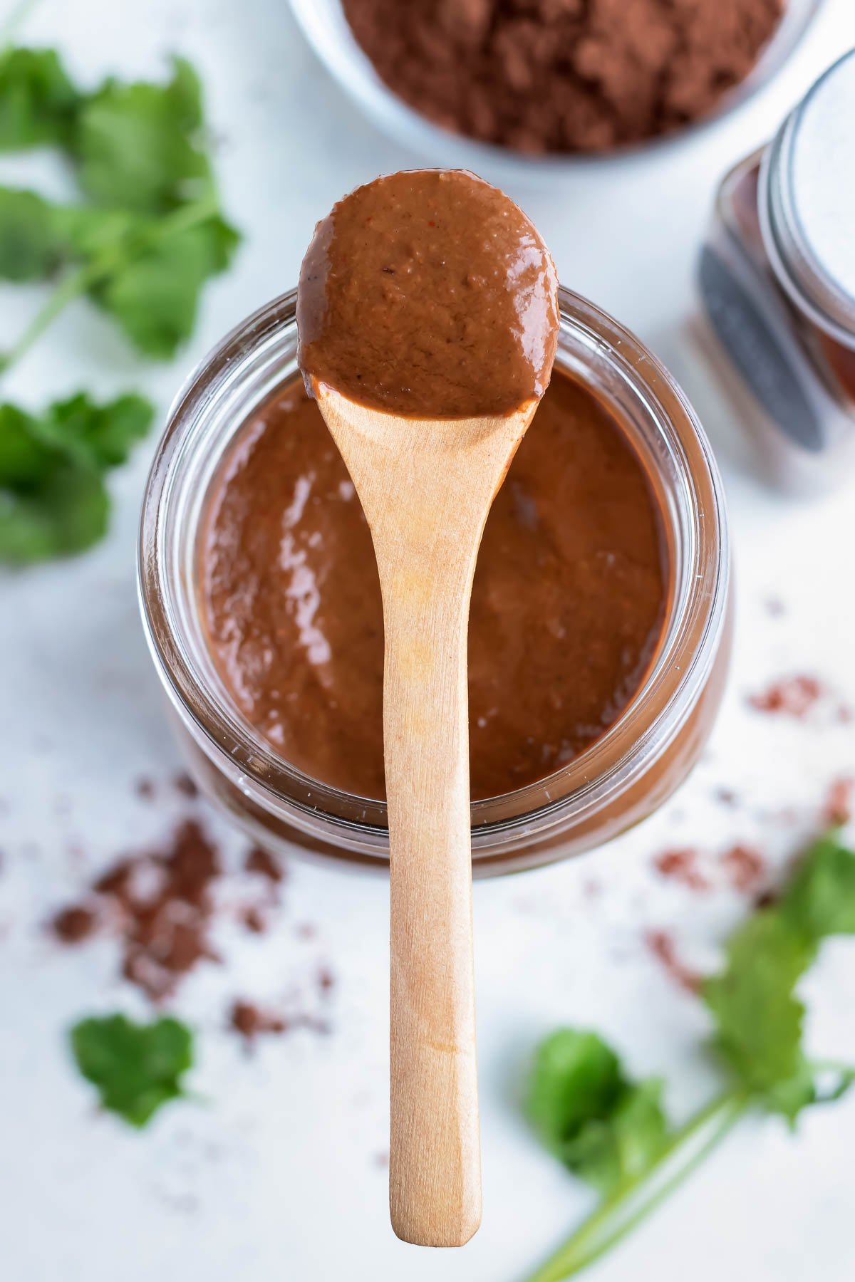 A spoon is used to serve mole sauce from a jar.