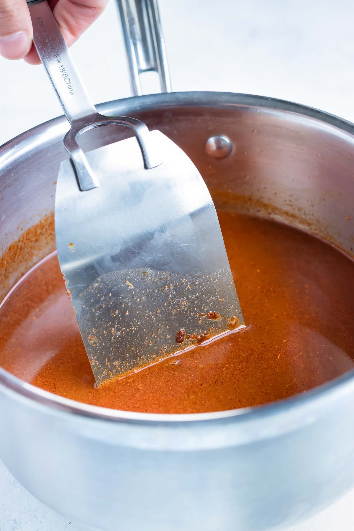 The chicken broth is added to the pan and stirred with a spatula.