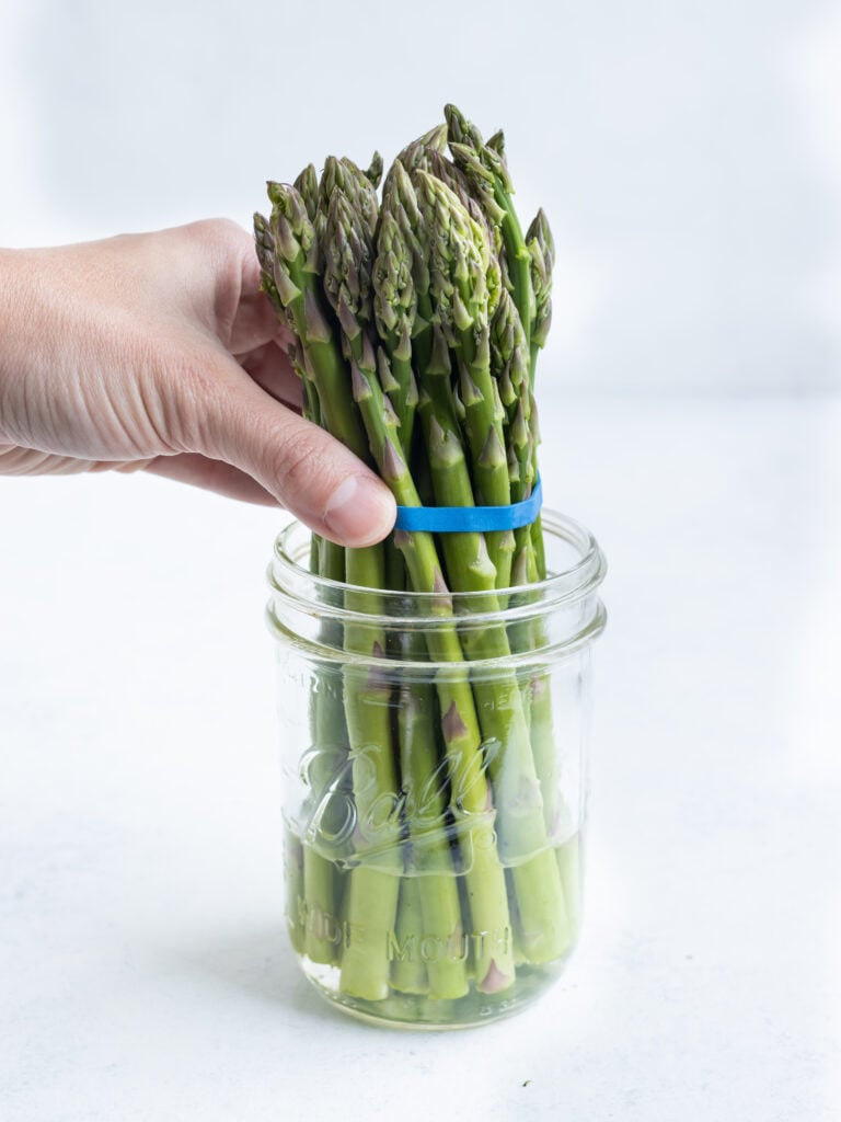 One bunch of asparagus sitting in a mason jar with water.