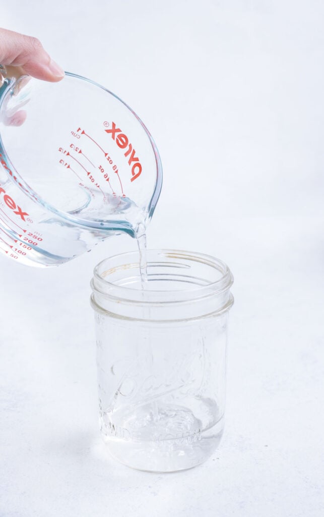 A clear glass measuring cup pouring water into a mason jar.