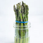 One bunch of asparagus sitting in a mason jar with water.