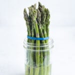 One bunch of asparagus sitting in a mason jar with water.