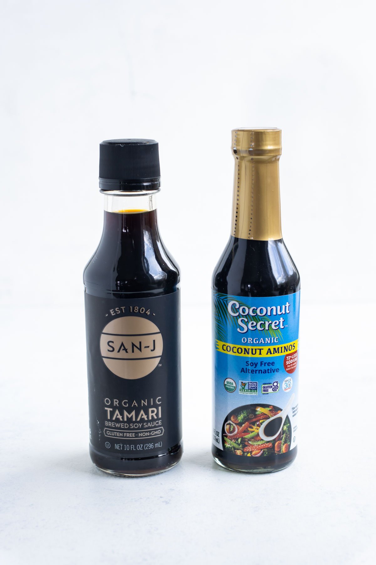 Coconut aminos and tamari bottles sitting next to each other on the counter top.