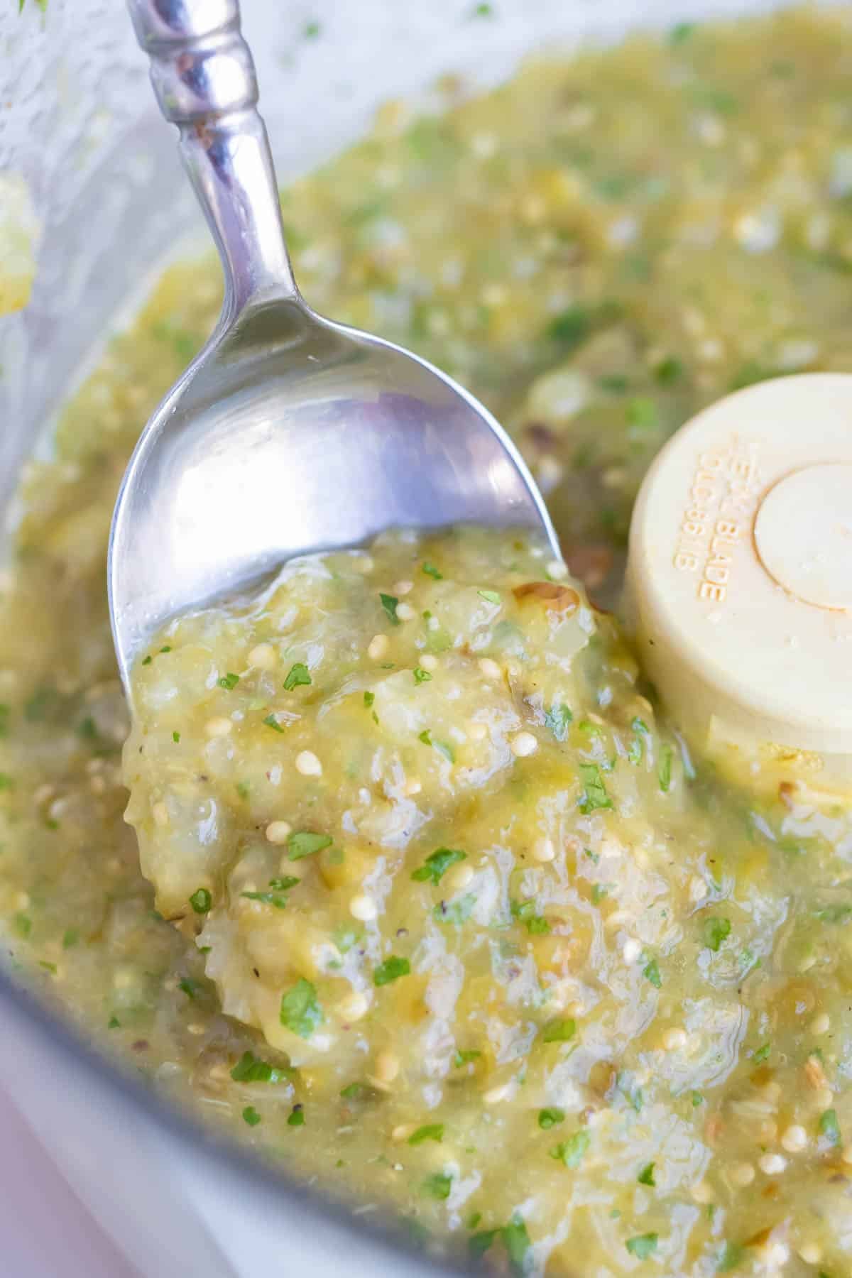 Tomatillo salsa is shown up close with a metal spoon.