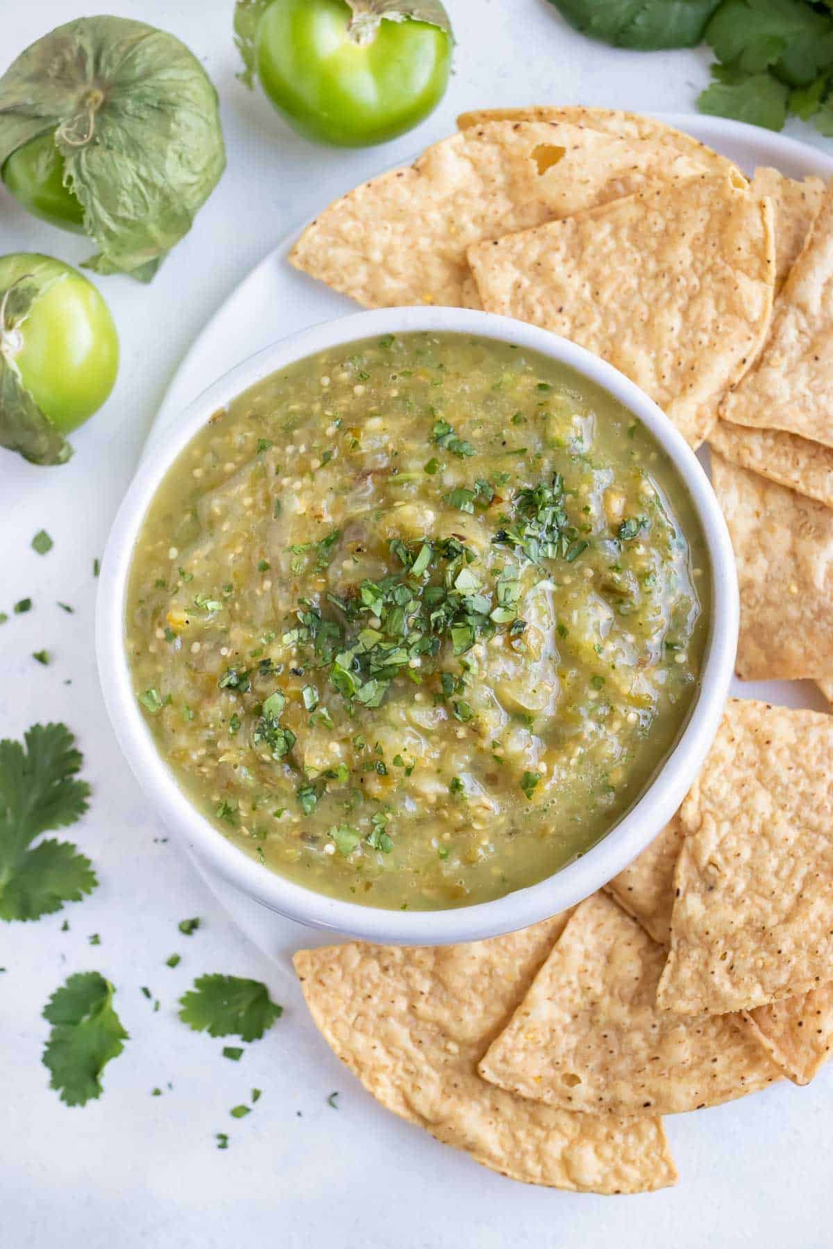 A bowl of tomatillo salsa verde is placed beside tortilla chips.