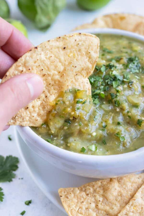 A chip is dipped into a big bowl of homemade salsa verde.