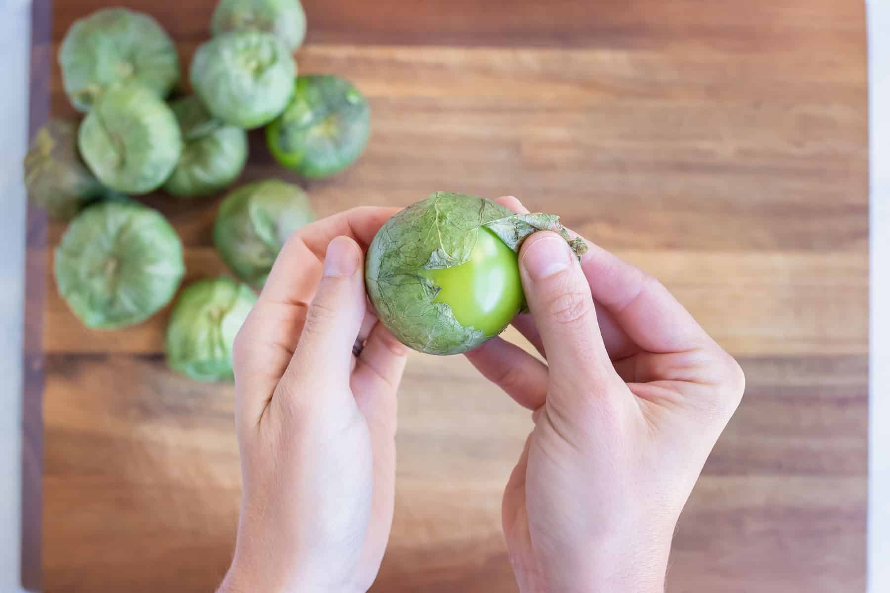 A hand removes the husk of a tomatillo.