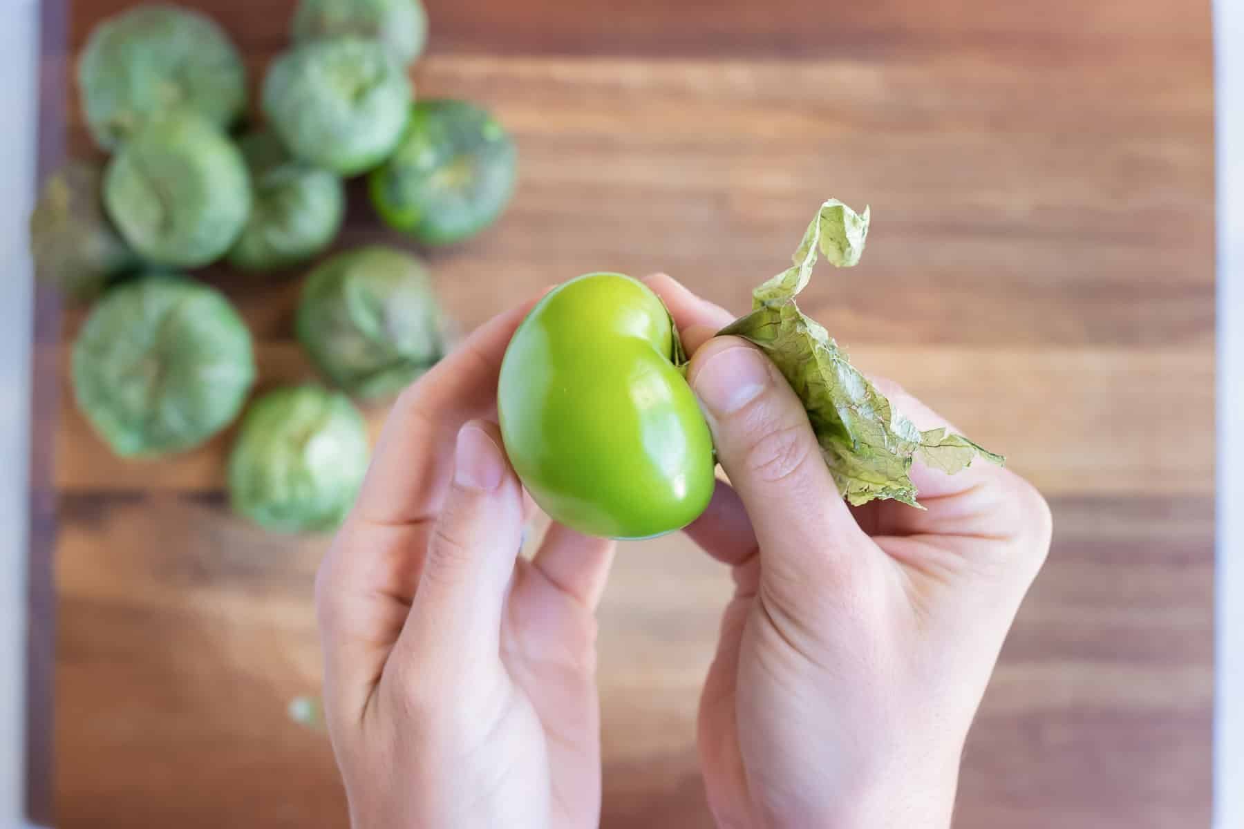 A hand removes the husk of a tomatillo.