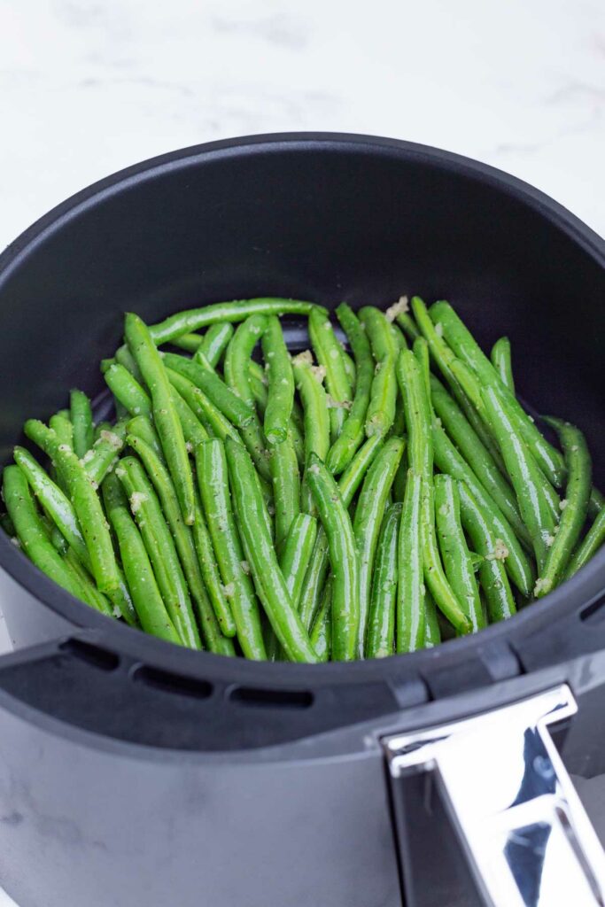 Seasoned green beans are added to the air fryer.