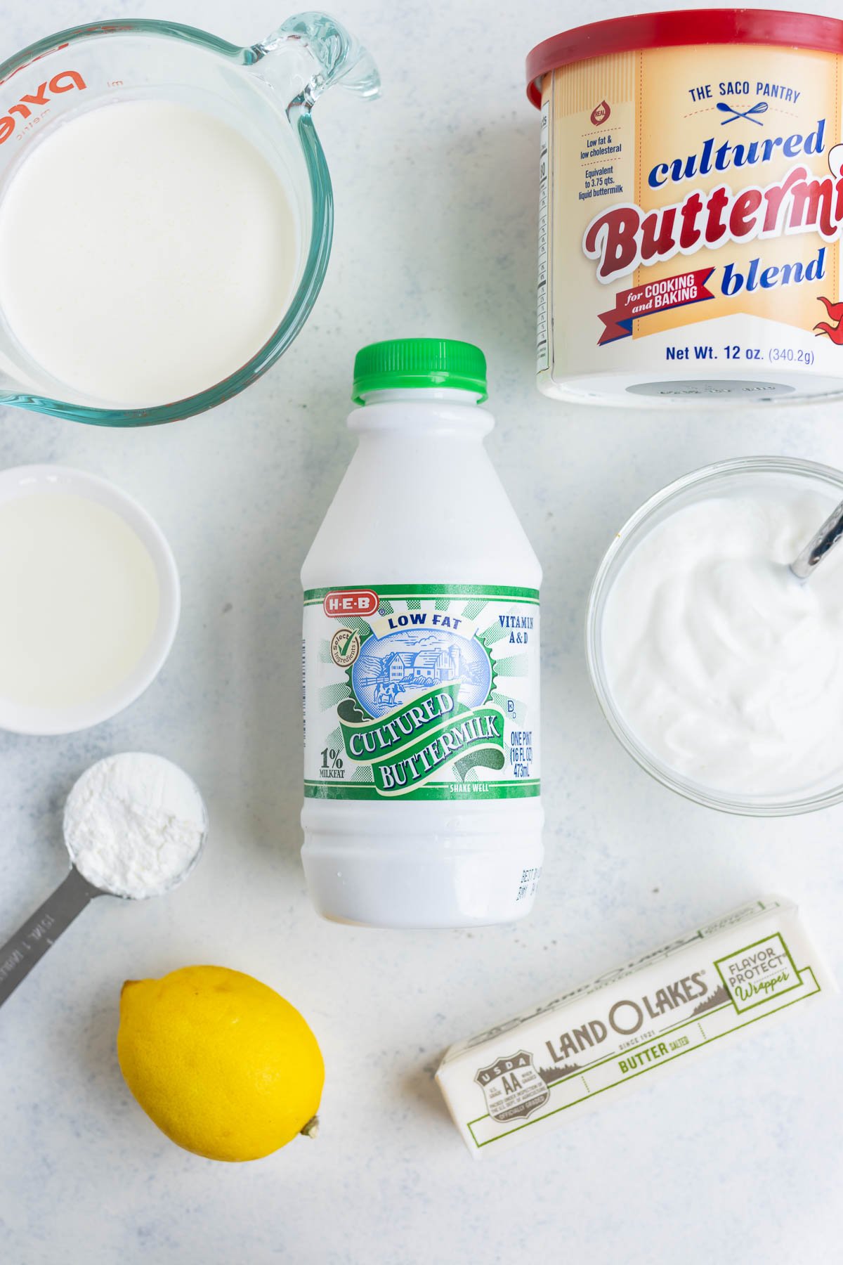 Buttermilk in its original container lying on the countertop with a lemon, butter, and other substitutes surrounding it.