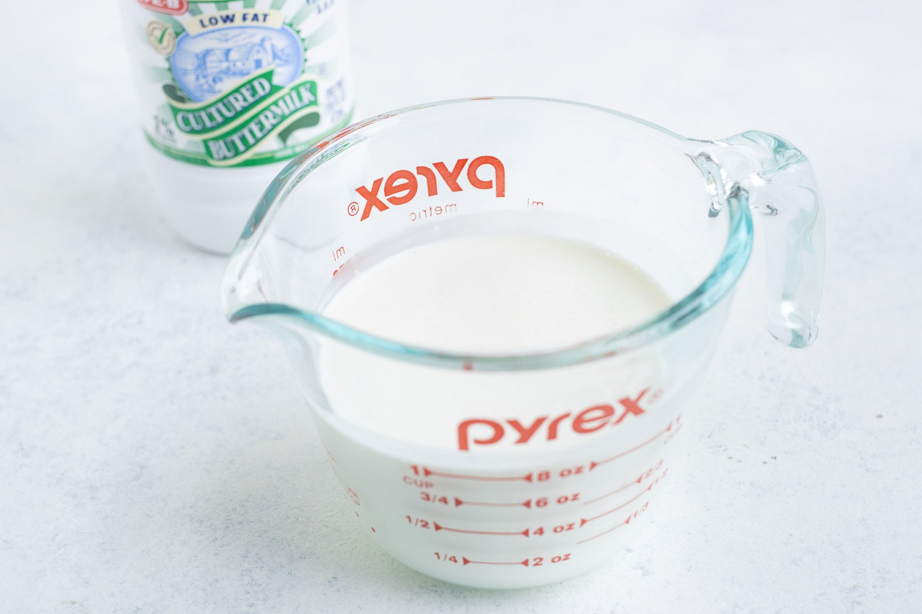 Buttermilk poured into a glass measuring cup with the original buttermilk container in the background.