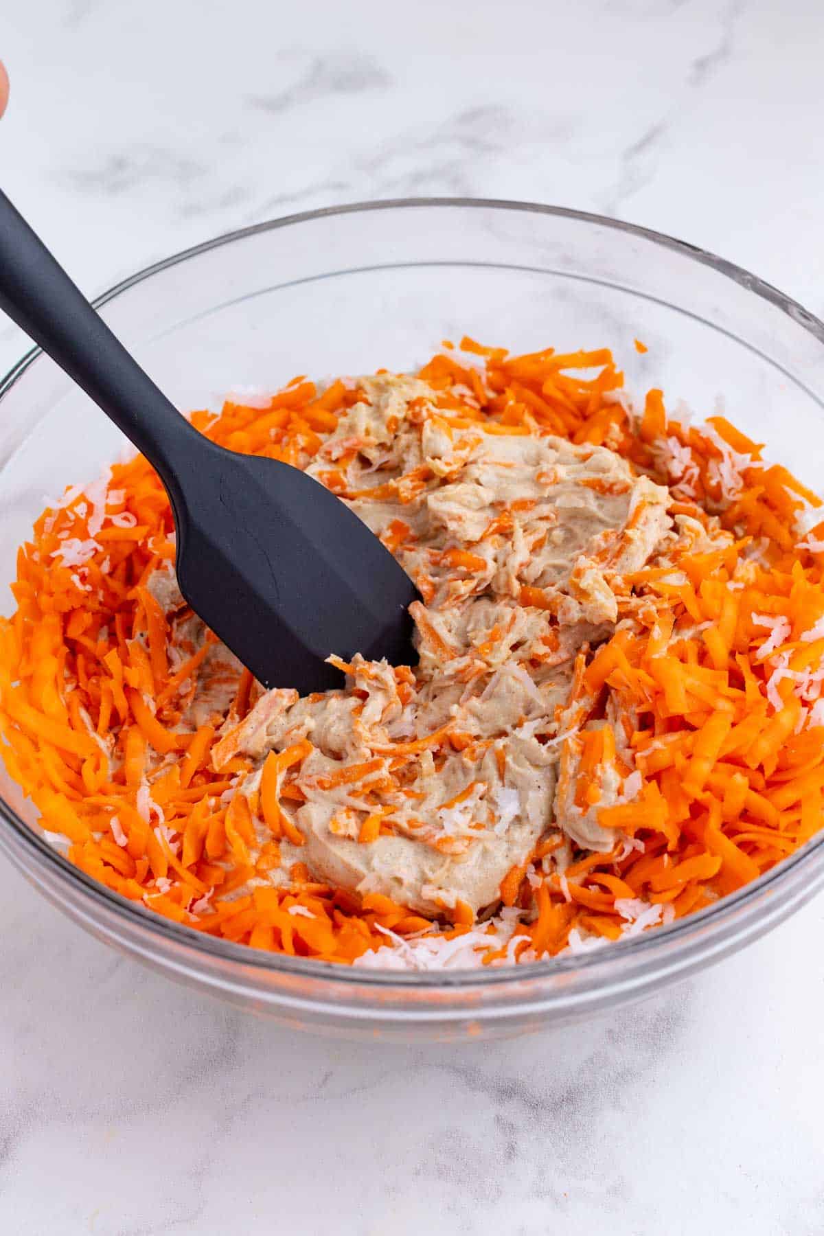A spatula folds in the carrots and coconut.