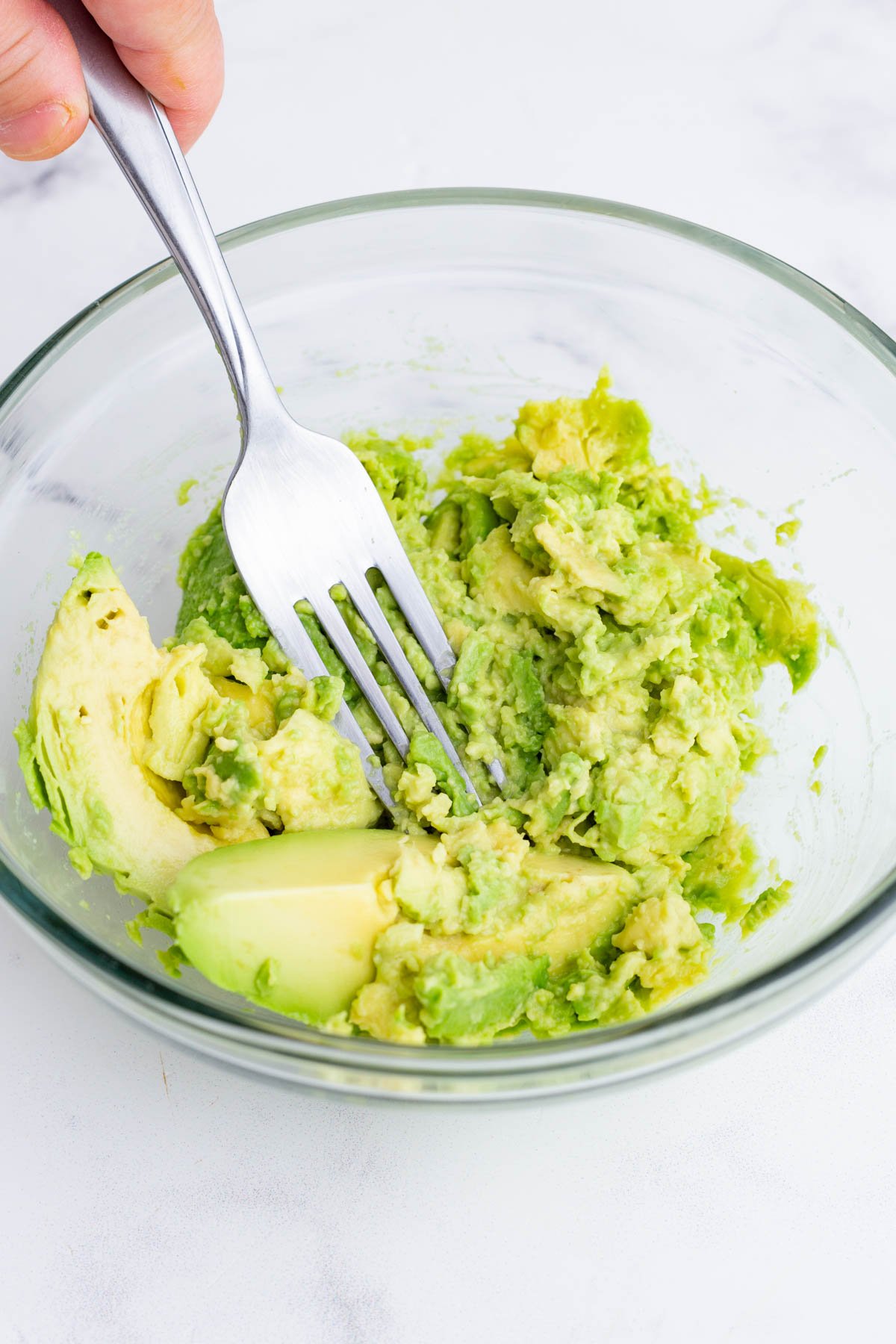 Avocados are mashed with a fork in a bowl.