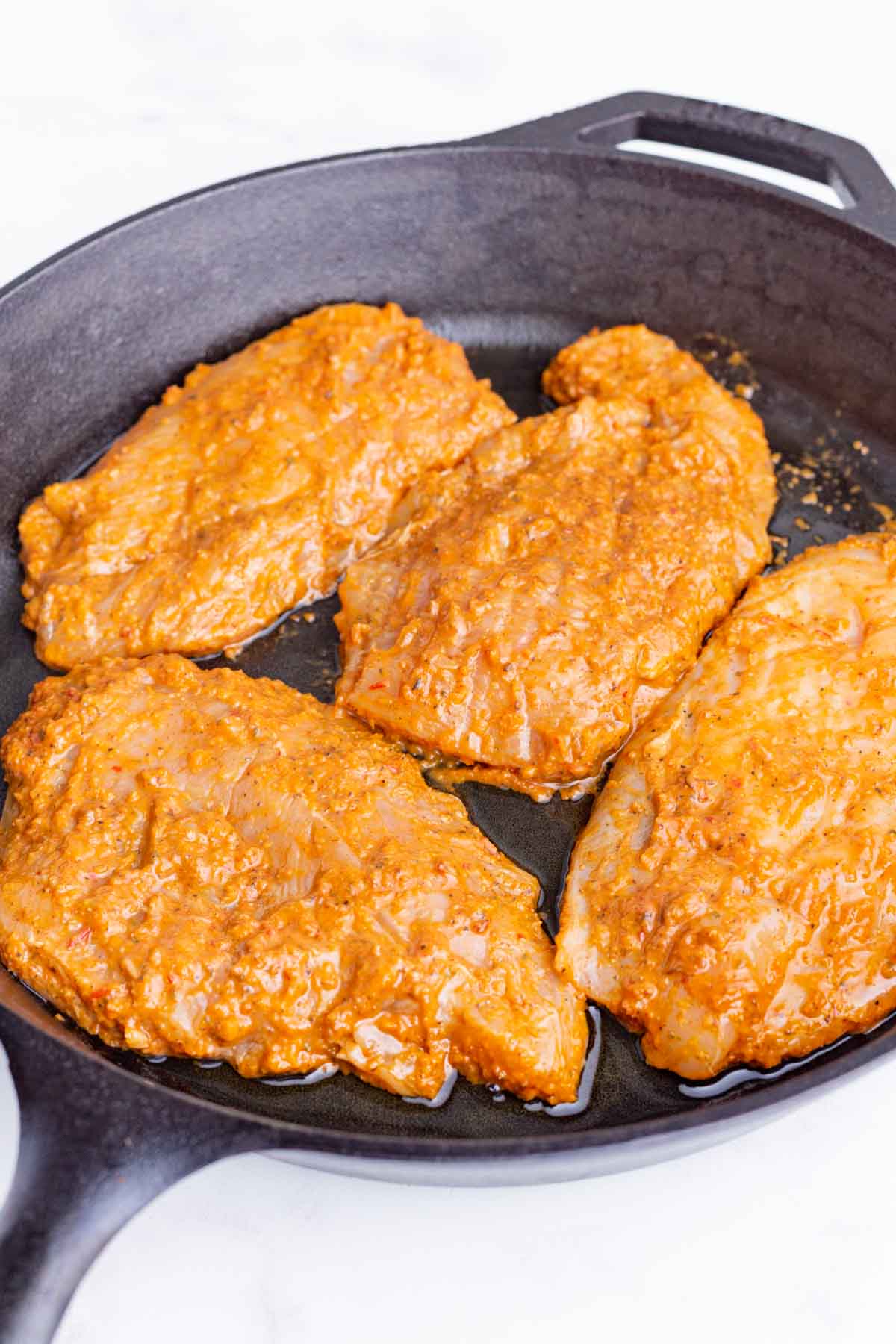 Marinated chicken breasts are cooked in a skillet.