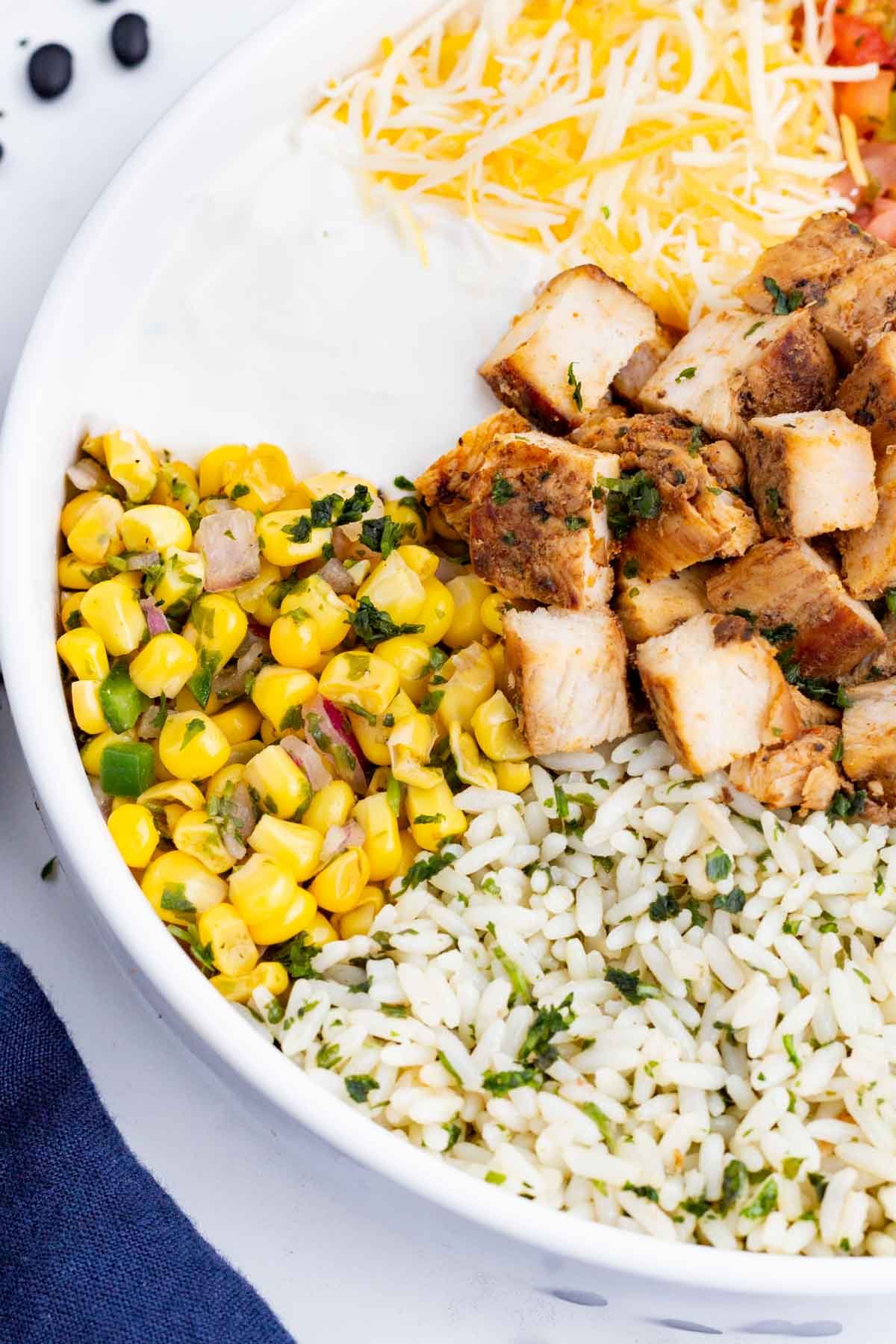 Corn salsa is piled into a burrito bowl with chicken, rice, and cheese.