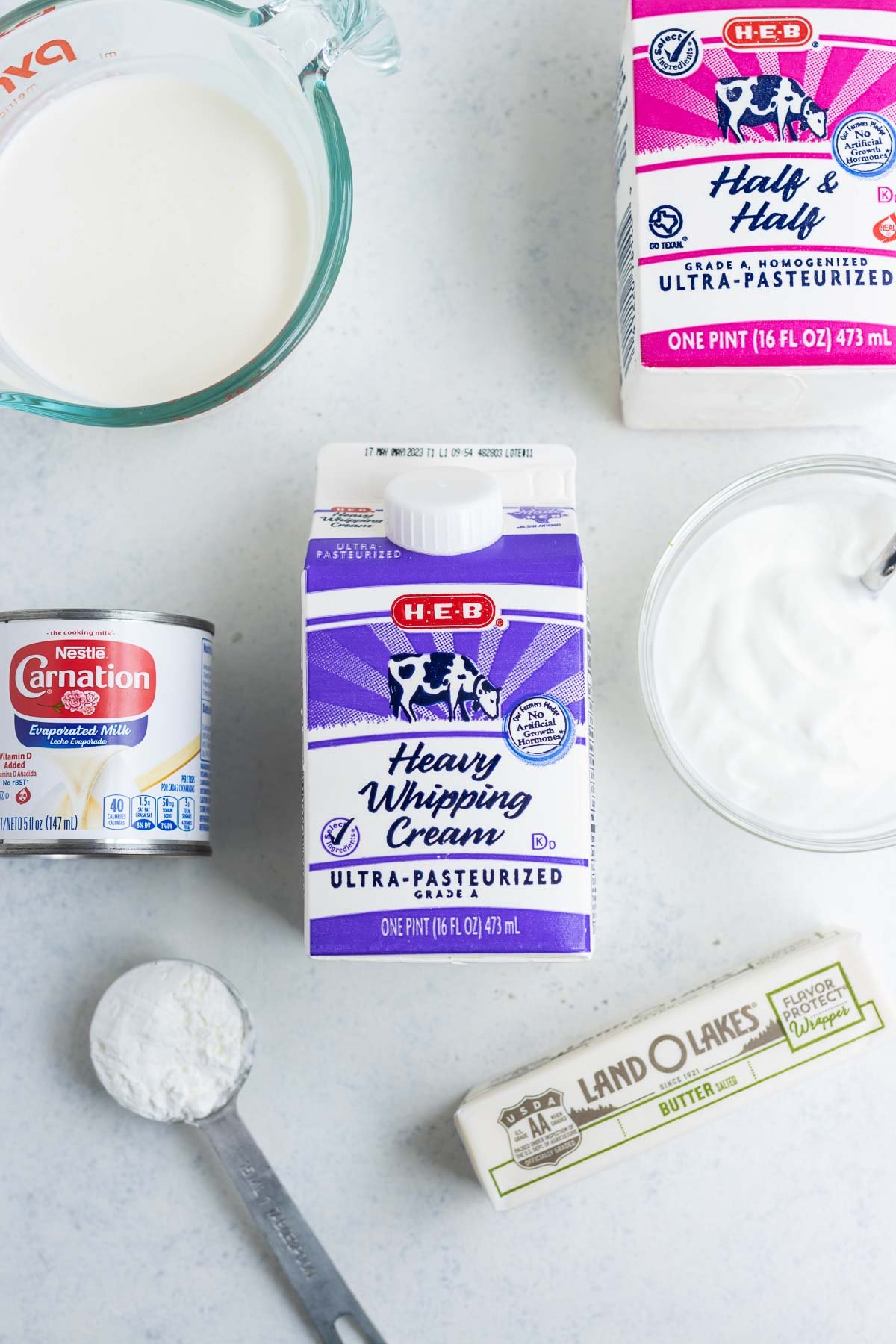 Heavy whipping cream laying on the countertop with its substitutes like butter and milk in the background.