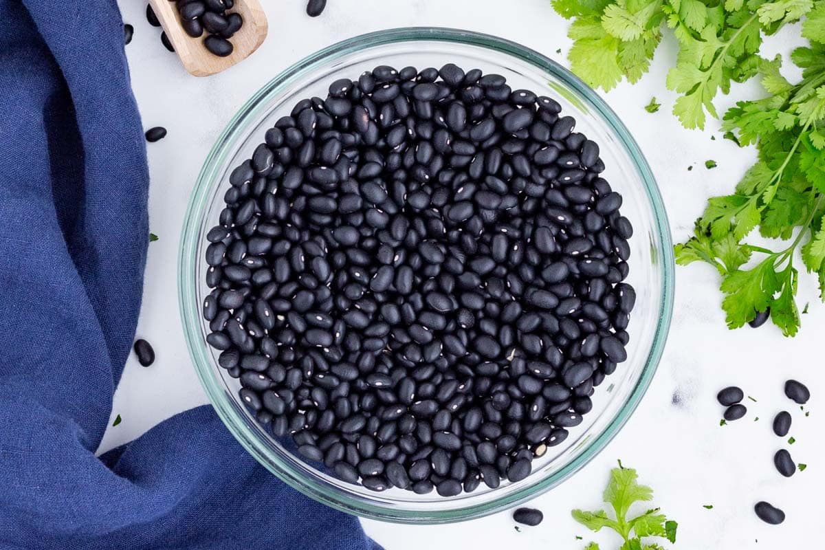 A clear bowl is full of dried black beans.