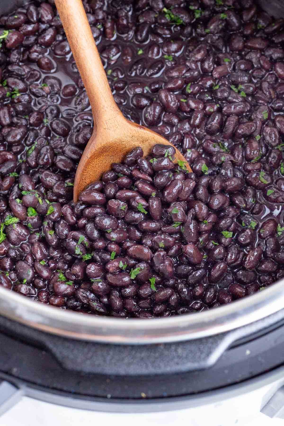 A spoon scoops cooked black beans out of an Instant Pot.