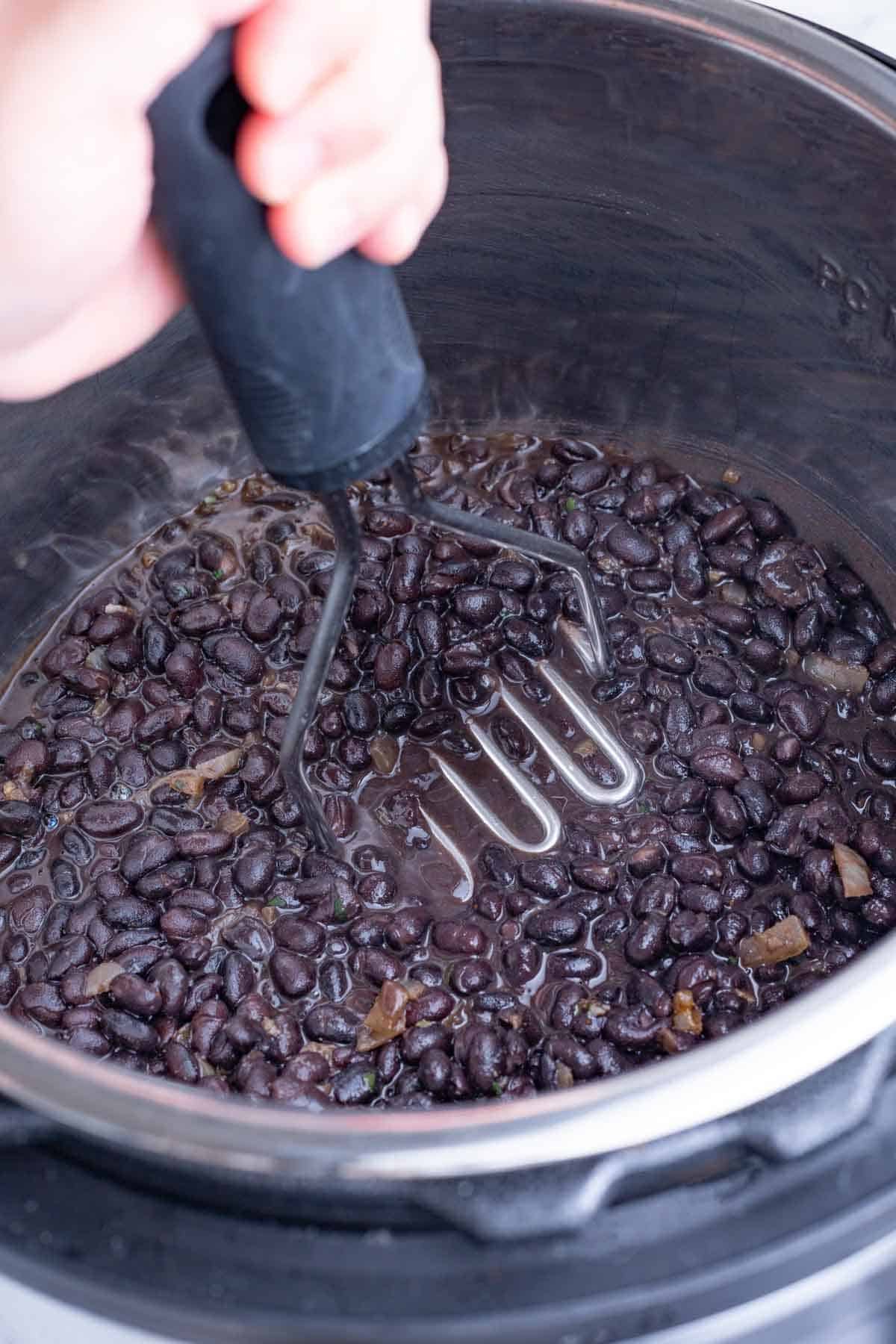 A potato masher is used to mash the black beans.