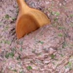 A wooden spoon stirs refried black beans in an Instant Pot.