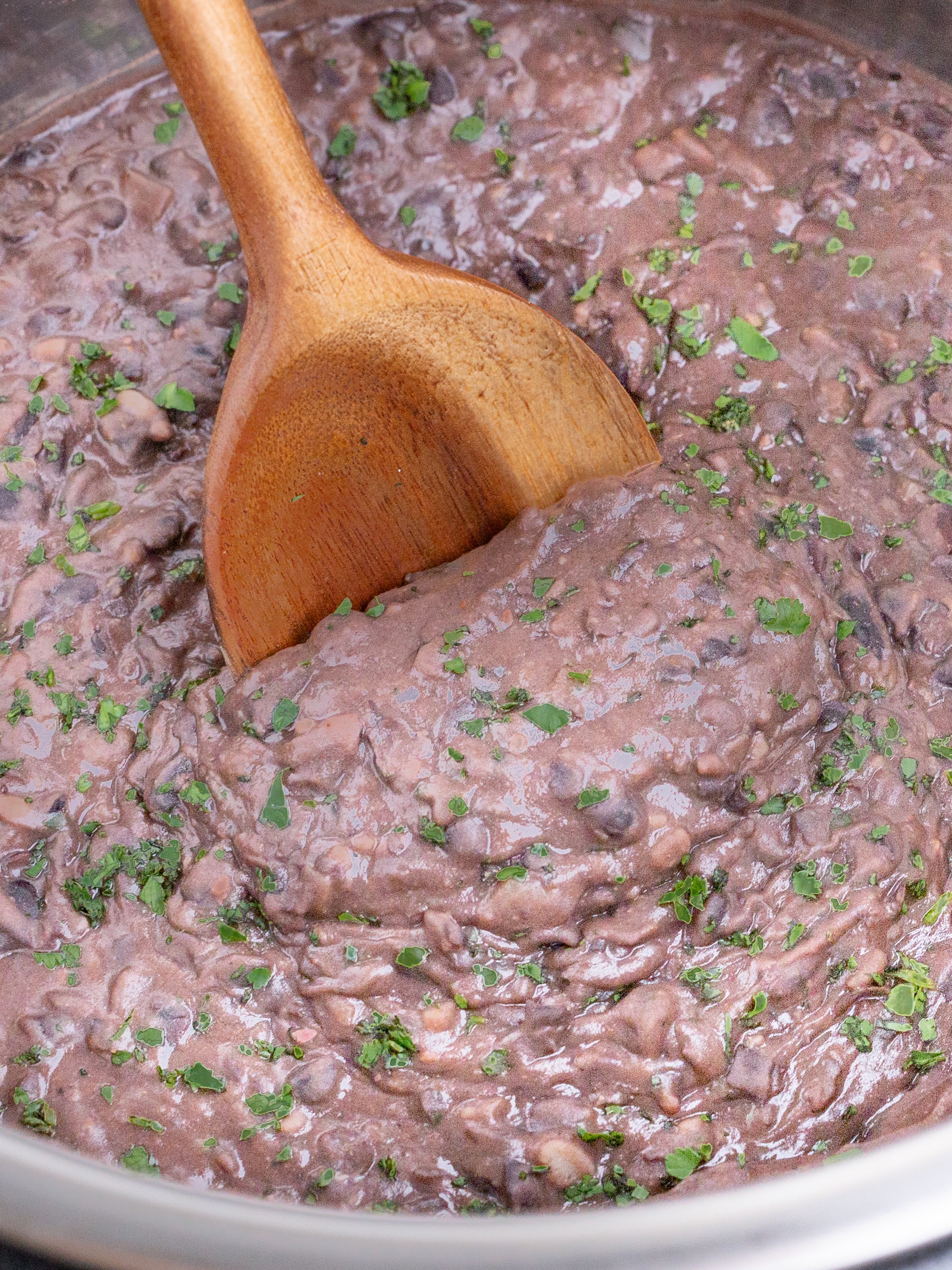 A wooden spoon stirs refried black beans in an Instant Pot.