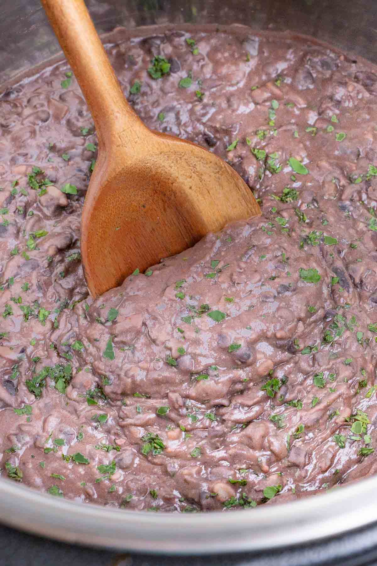 A wooden spoon stirs refried black beans in an Instant Pot.