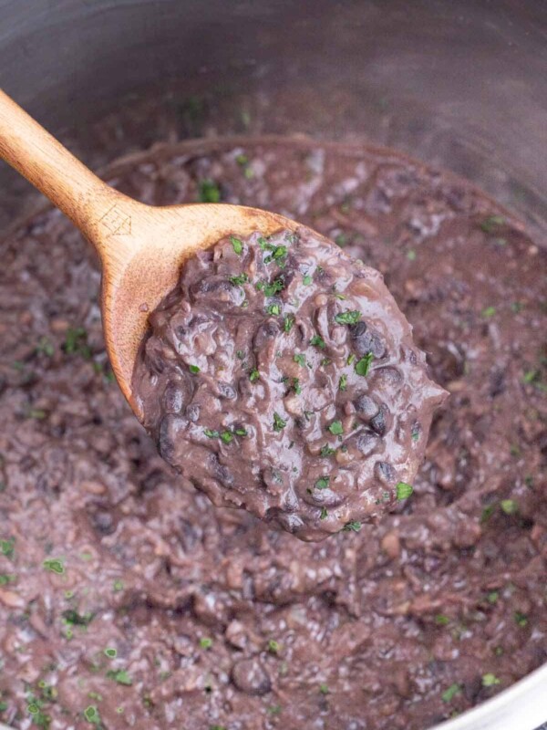 A spoon scoops cooked refried black beans out of an Instant Pot.