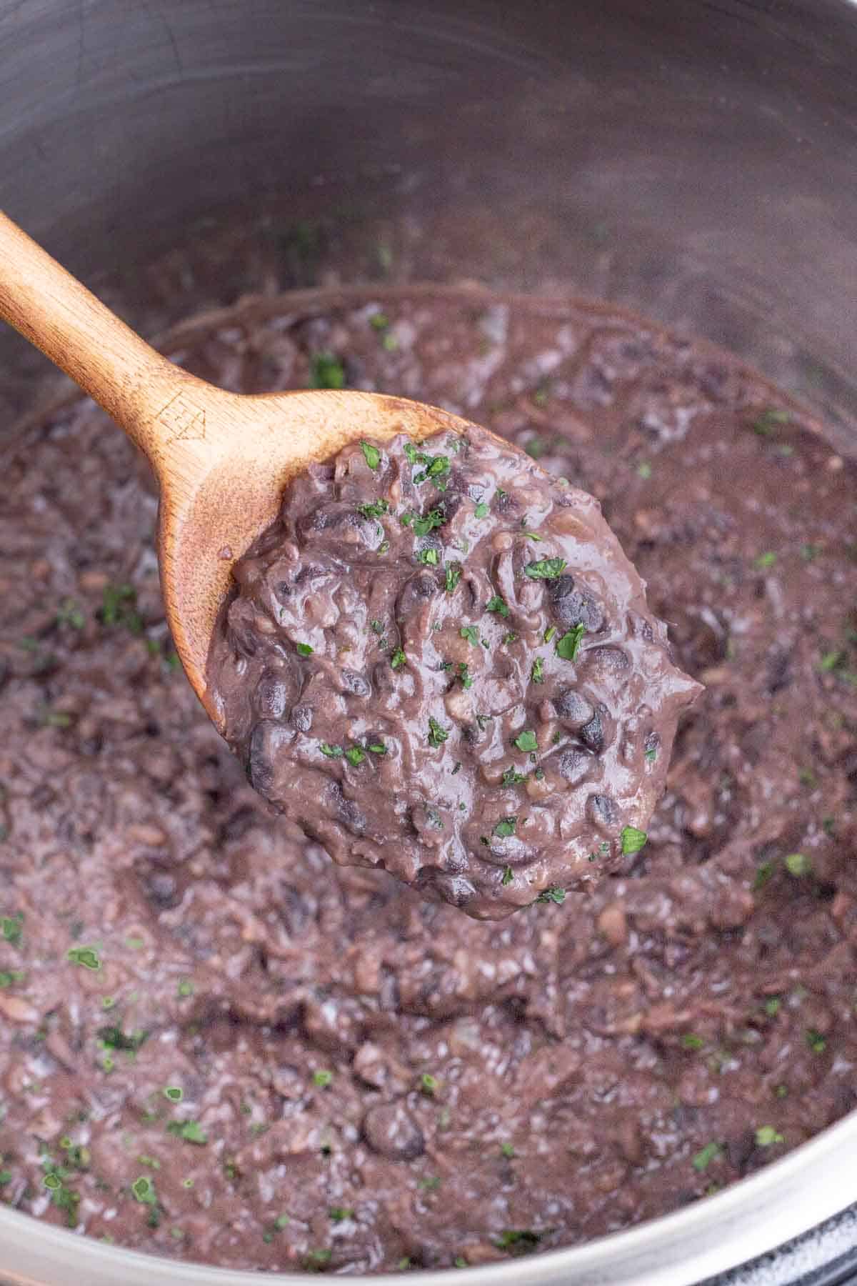 A spoon scoops cooked refried black beans out of an Instant Pot.