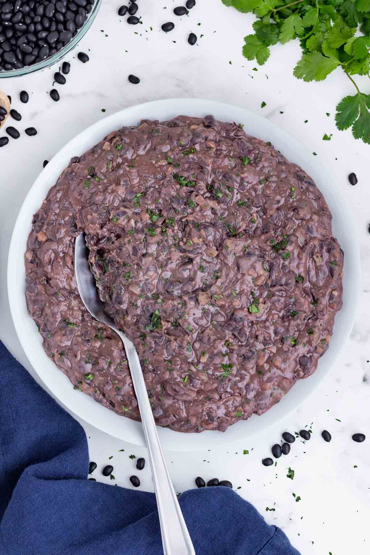 A spoons scoops refried black beans out of a white bowl.