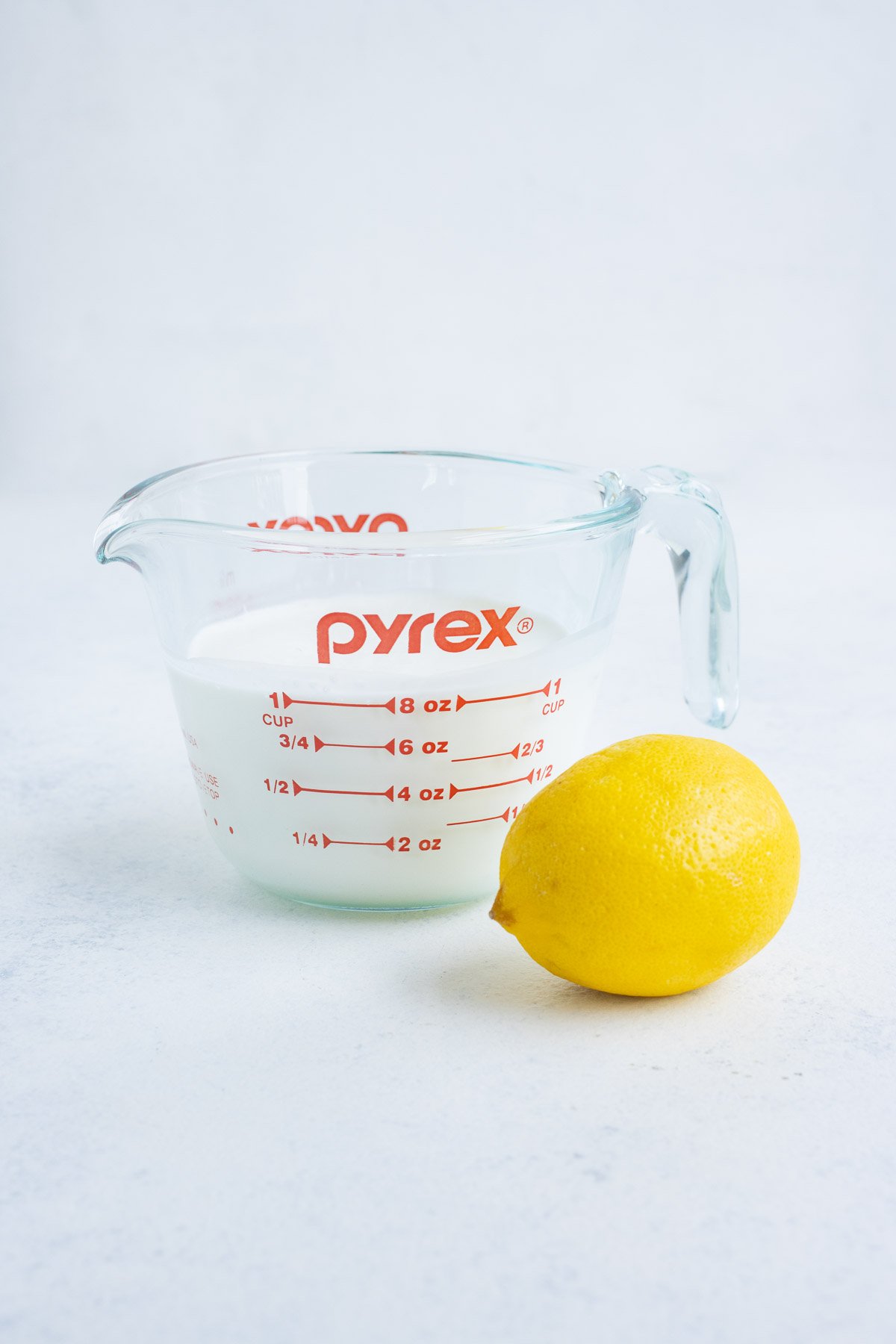 Milk in a glass measuring cup with a lemon on the side.