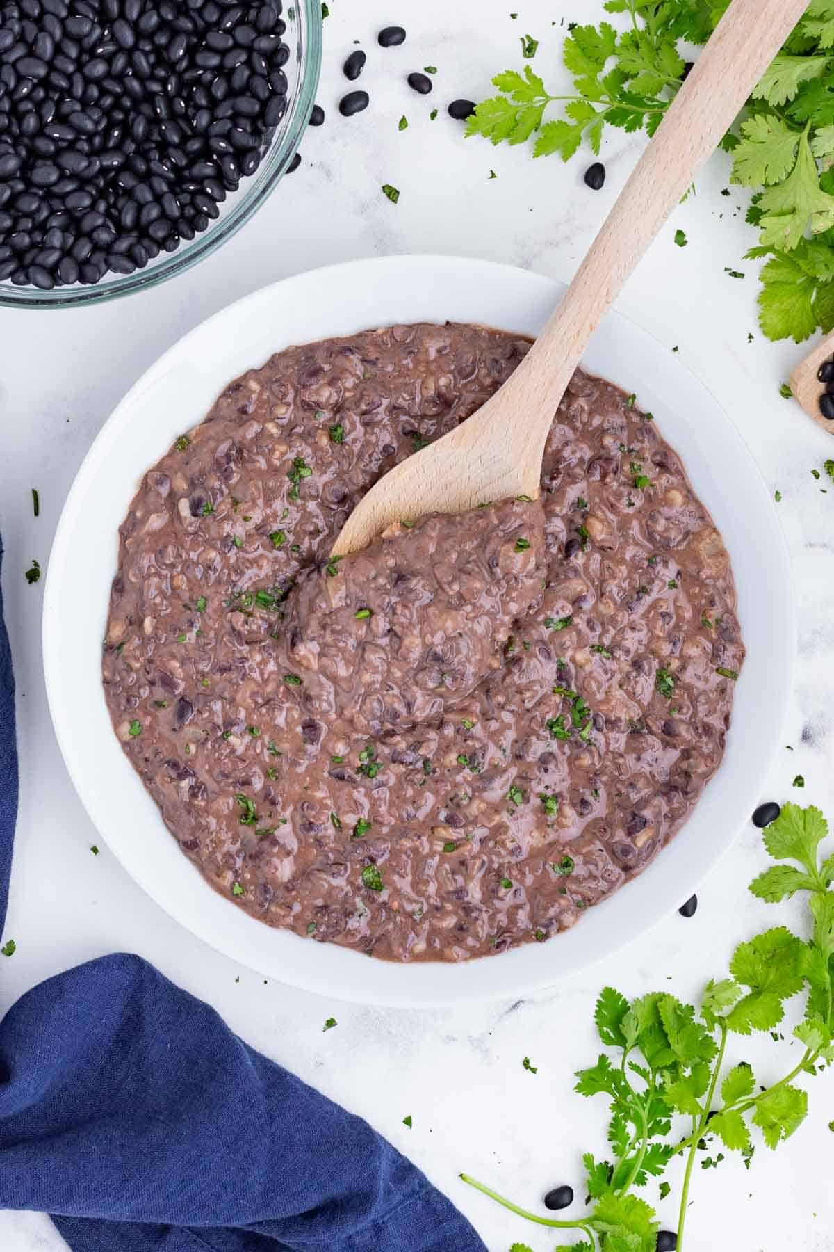 A spoons scoops refried black beans out of a white bowl.