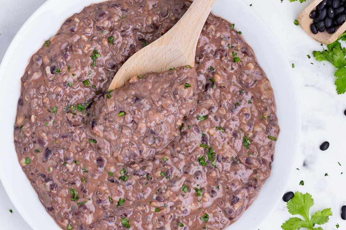 A wooden spoon stirs refried black beans made from canned beans.