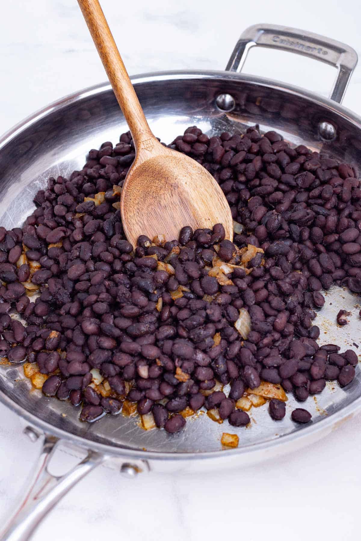 Cooked black beans are added back into the skillet with the onions.