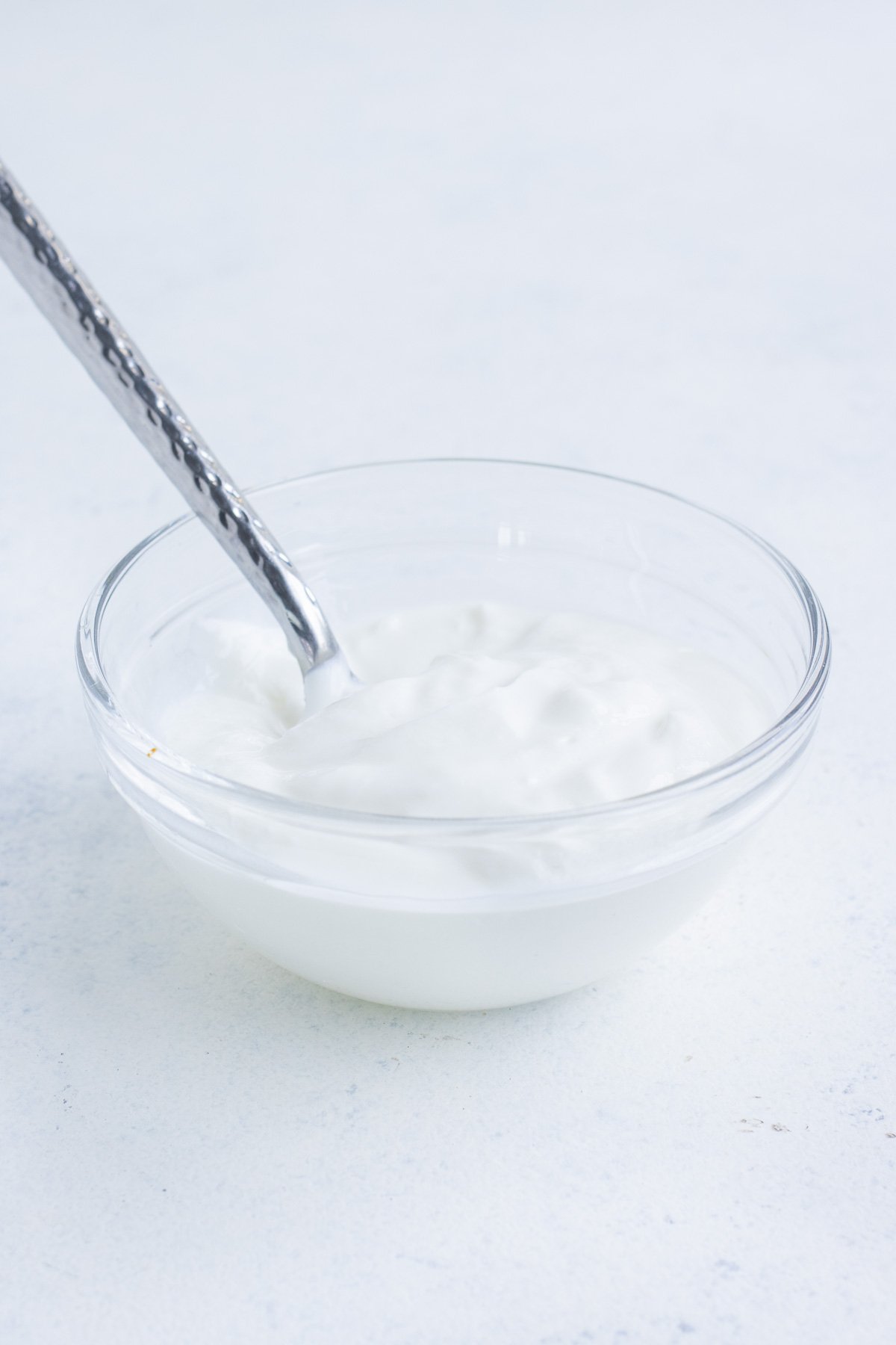 Glass bowl with sour cream and a spoon in it.