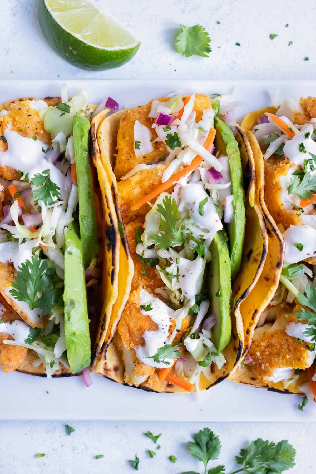 Three fish tacos are served side by side on a white plate for dinner.