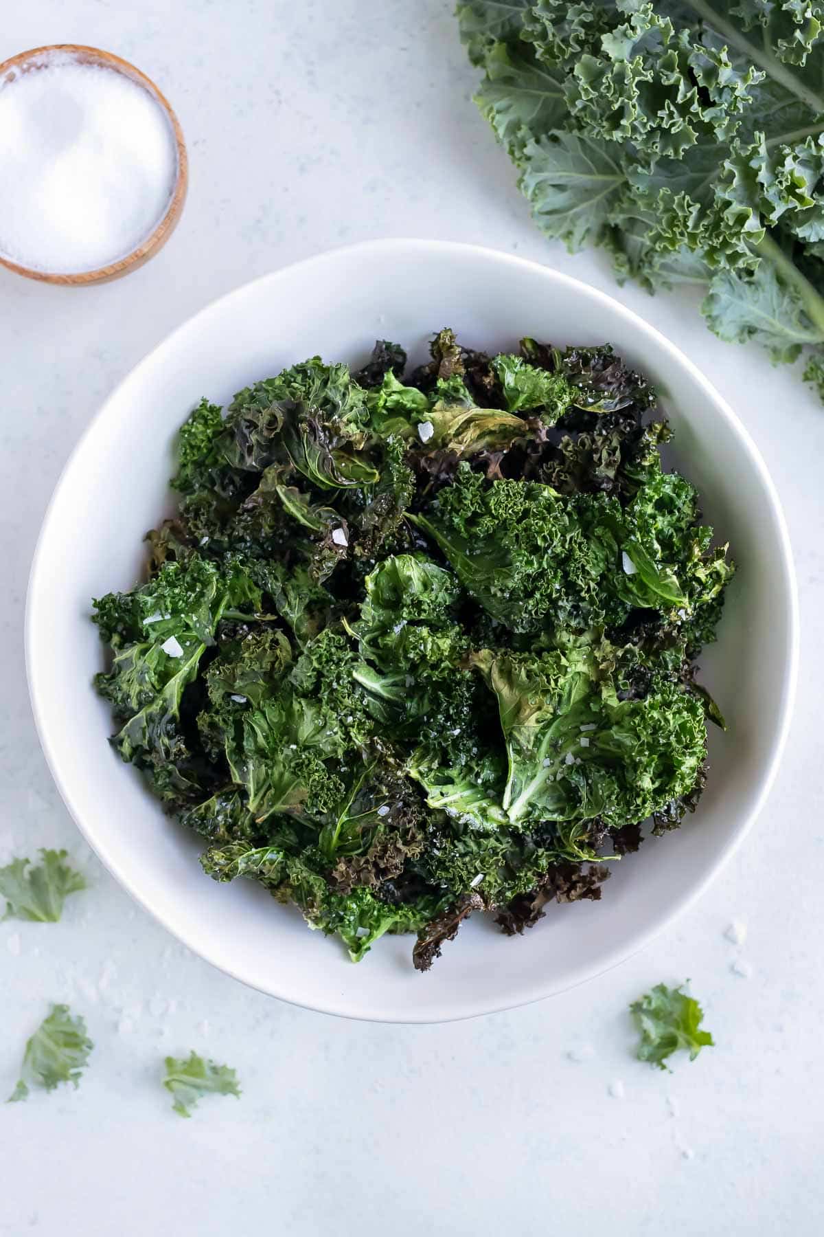 An overhead shots shows a bowl of crunchy air fryer kale chips on the counter with fresh kale.