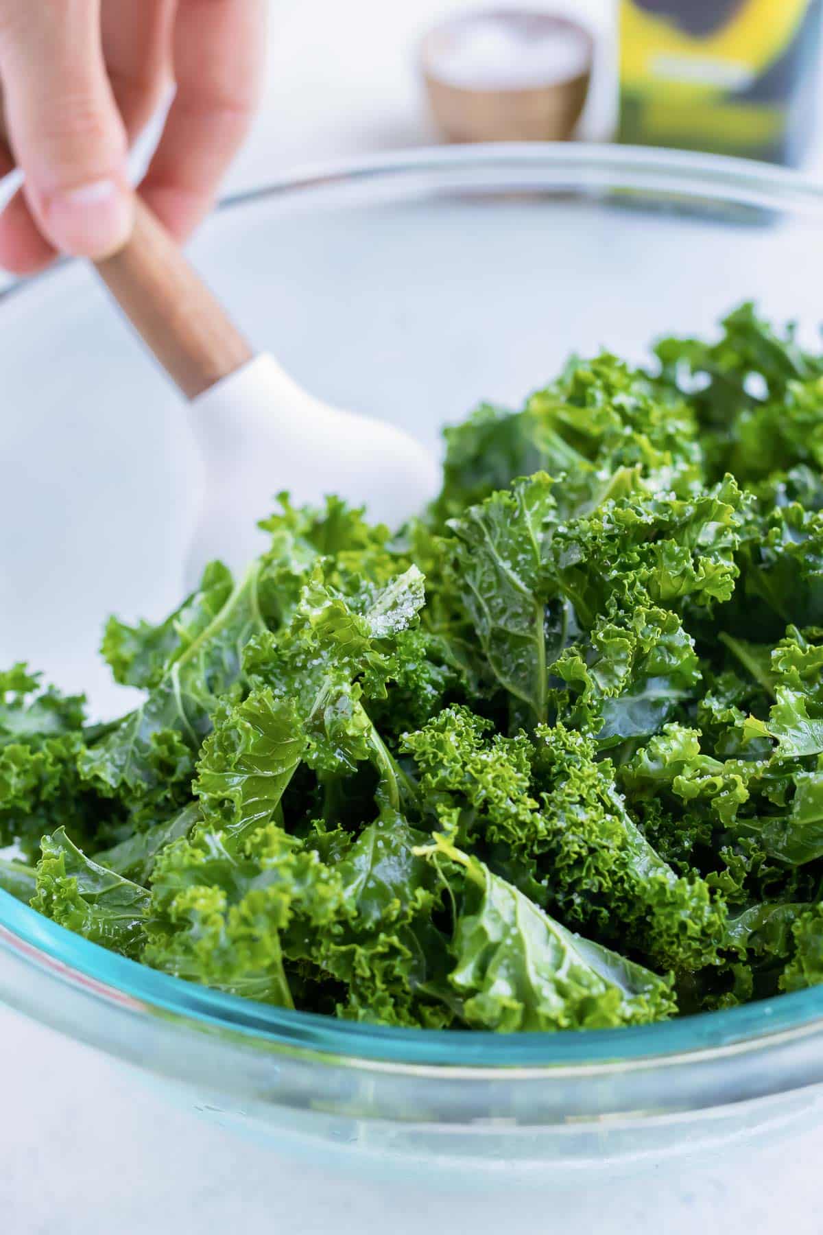 The prepared kale leaves are tossed with oil and salt in a bowl.