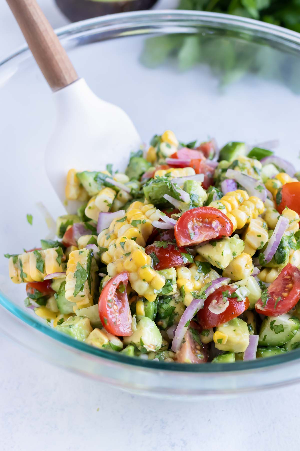 Summer avocado corn salad is mixed with the oil and lime juice with a spatula.