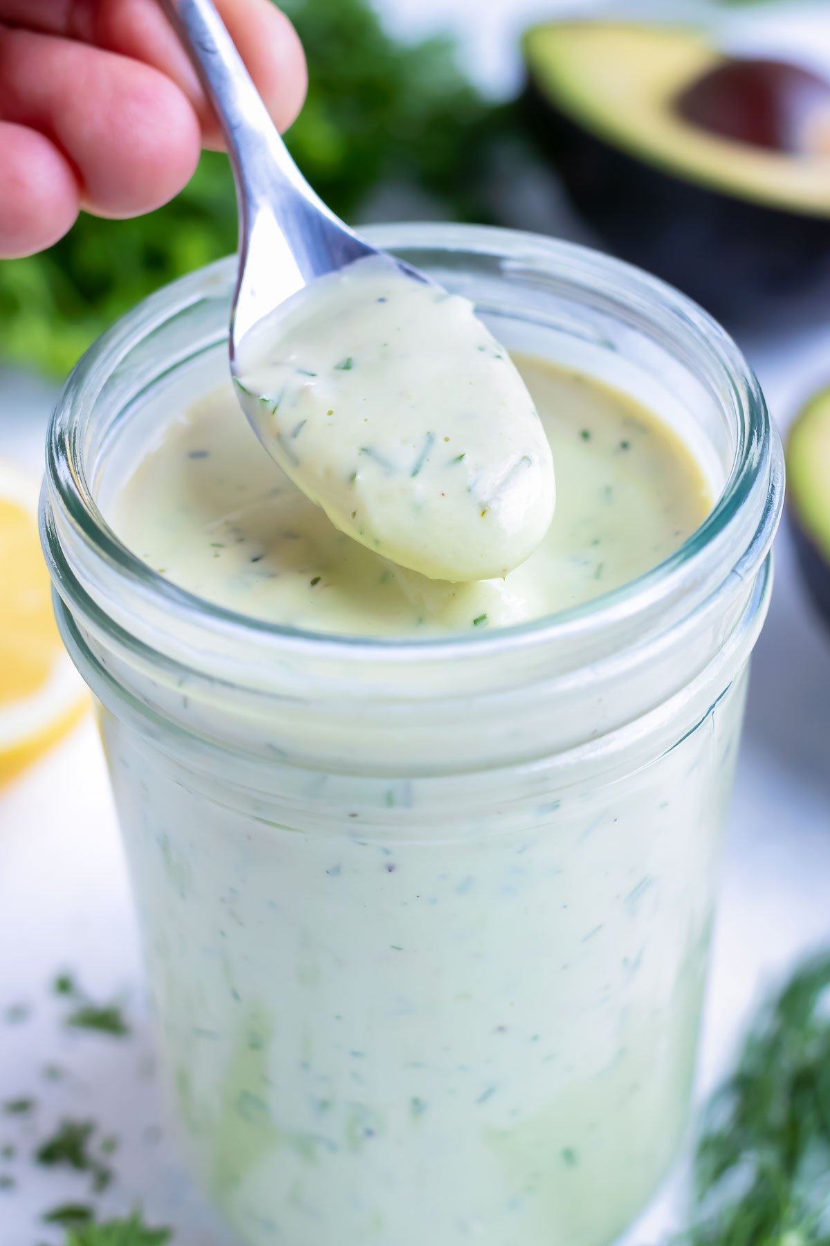 A spoon is shown lifting the avocado ranch dressing from the jar.